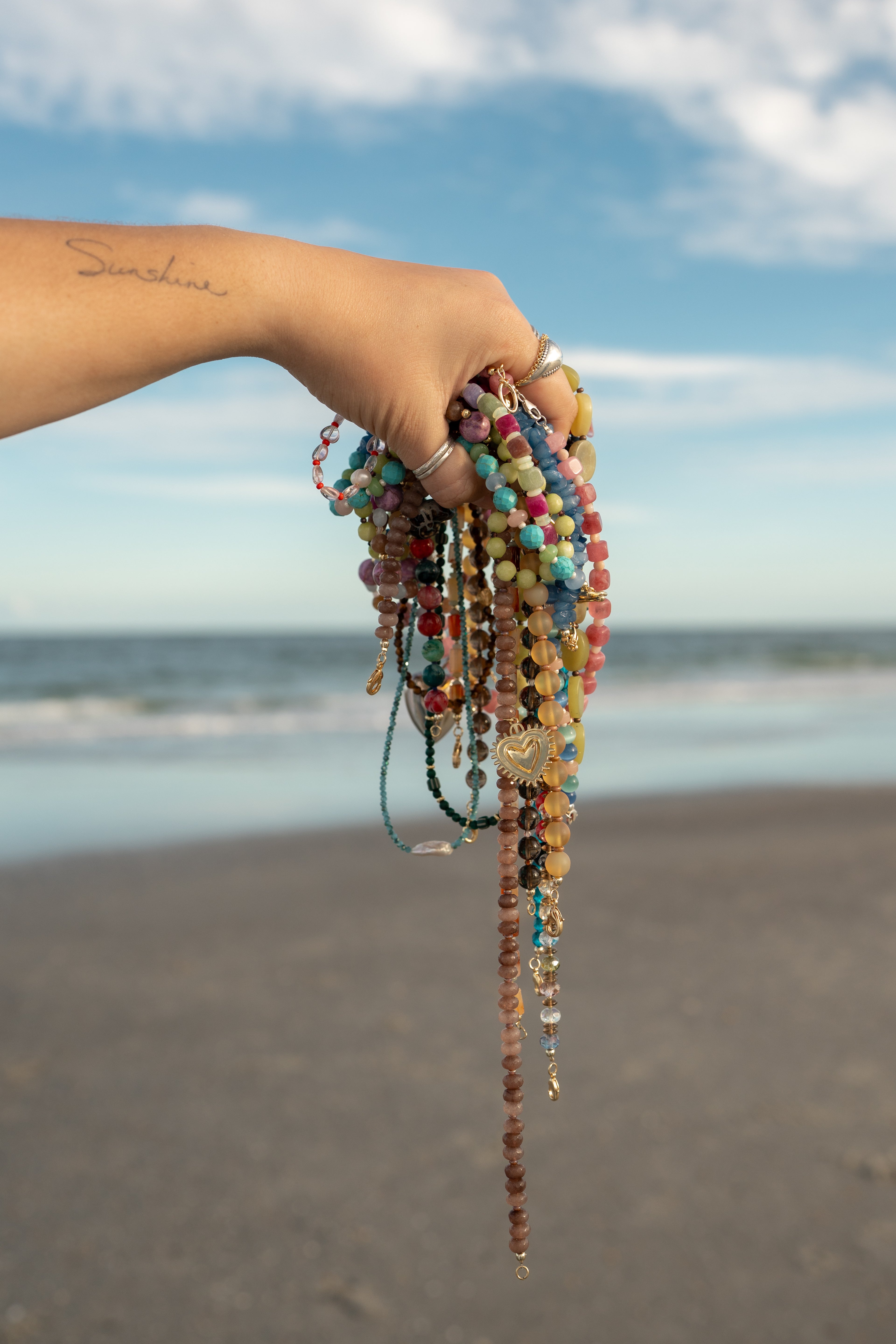 Hand holding colorful beaded bracelets with a beach and ocean in the background